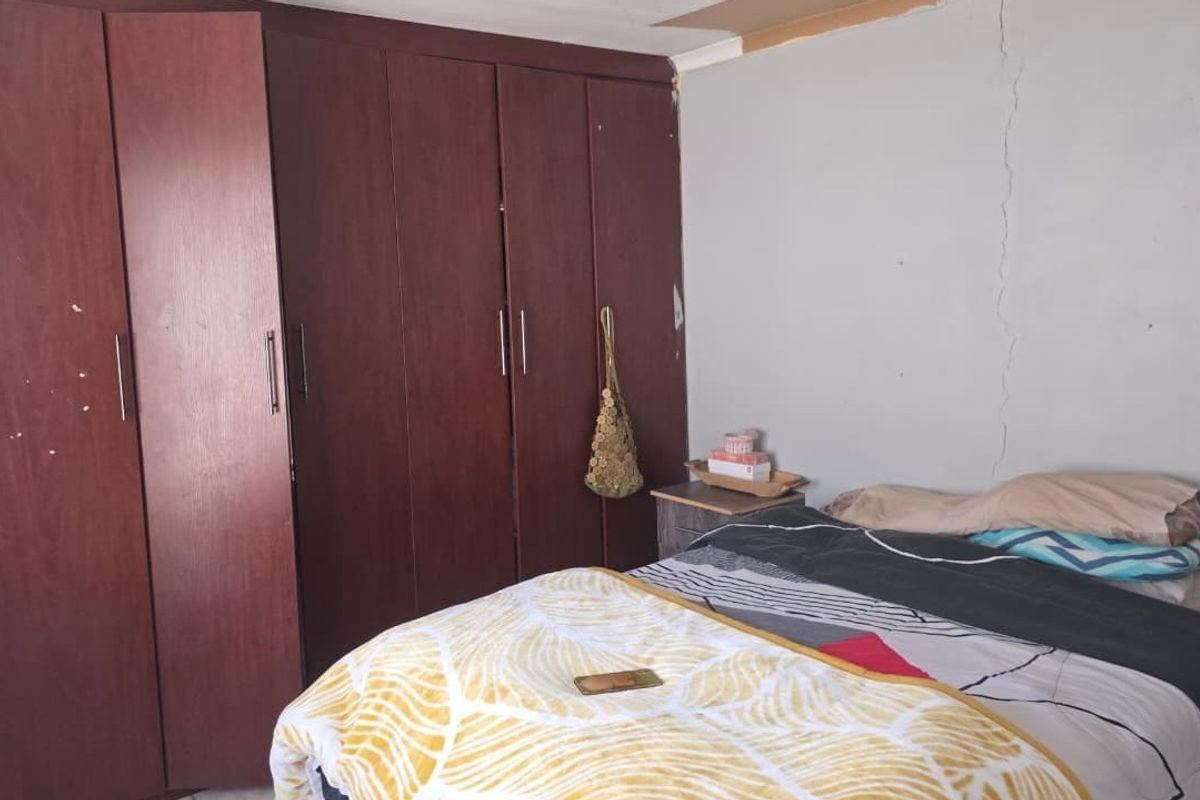 Bedroom featuring dark wood built-in cupboards, showing signs of wall cracking and ceiling damage requiring maintenance.