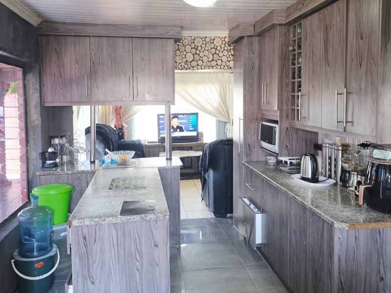 A functional kitchen featuring wood-look laminate cabinetry, granite countertops, a breakfast bar, and tiled flooring, with an open layout leading to the living area.