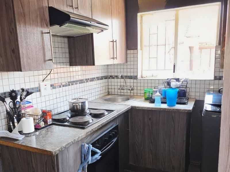 Compact kitchen featuring wood-look cabinetry, laminate countertops, built-in oven and hob, extractor fan, and tiled backsplash with a functional sink area.