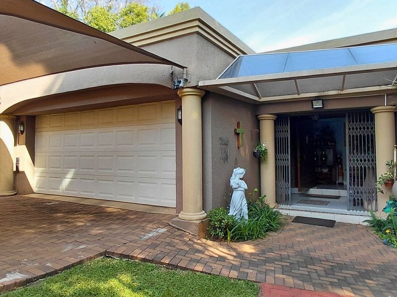 Front facade featuring a paved driveway, double garage, covered entrance with security gate, and a shade sail structure.