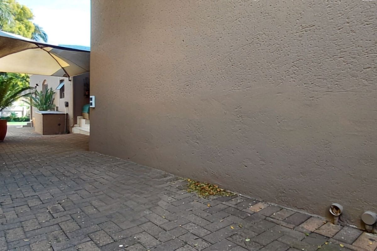 A side passage or rear exterior area featuring paved flooring, a textured wall, and a shade sail covering the walkway.