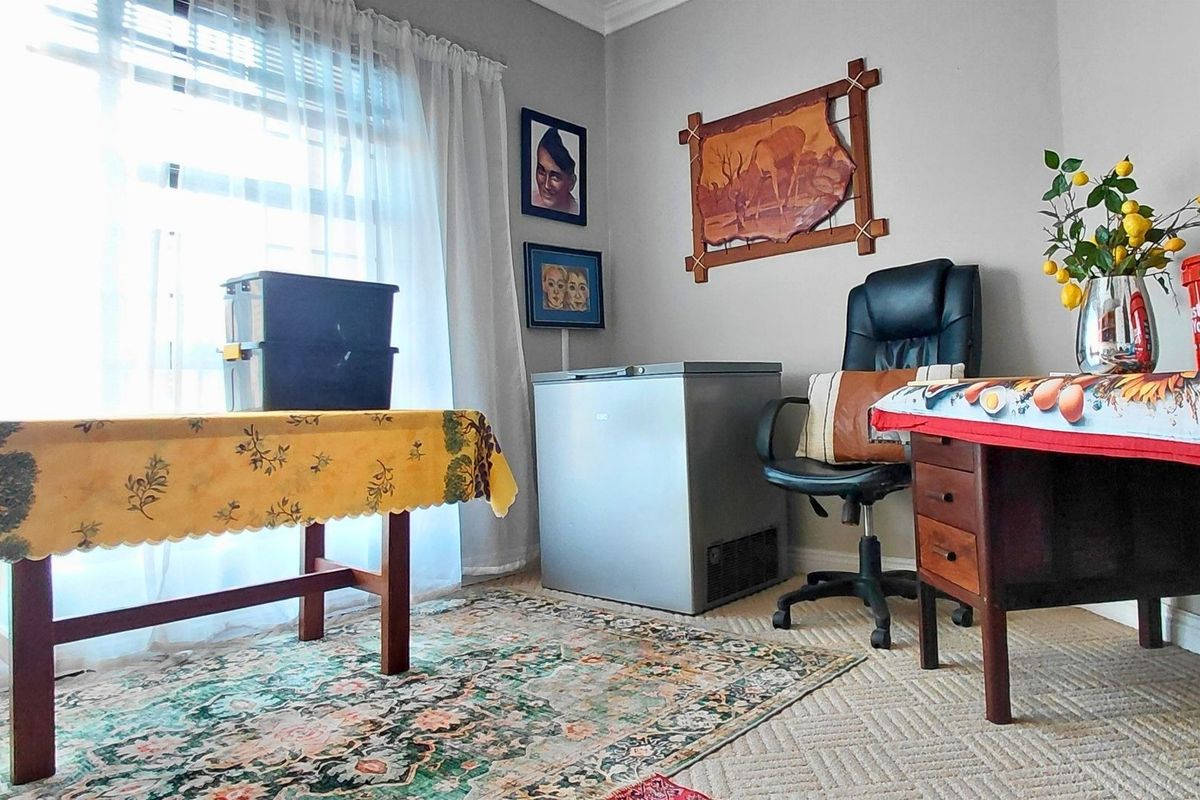 A multi-purpose room featuring carpeted flooring and natural light through a large window, currently utilized as a workspace and storage area.
