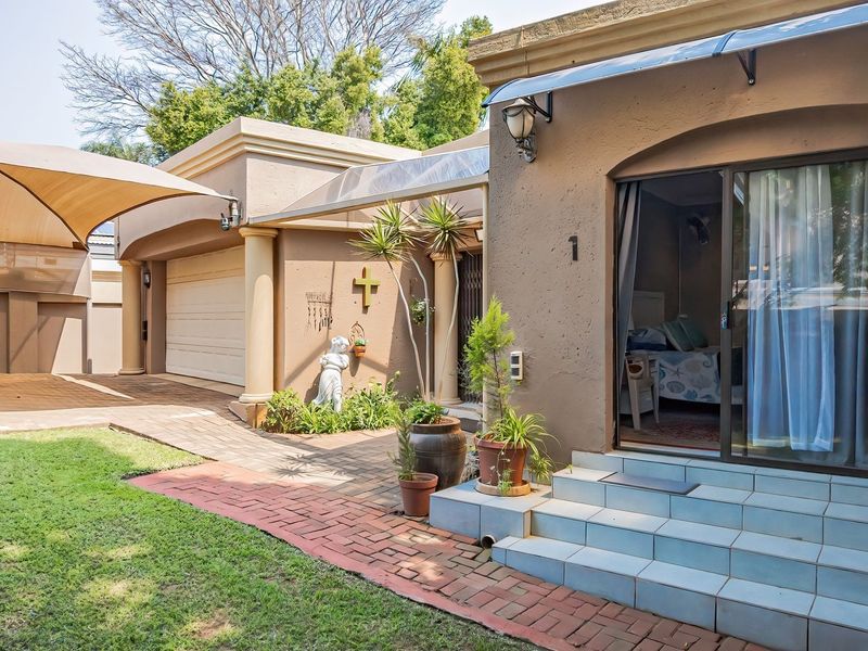 Rear exterior view featuring a paved driveway, shade sail, garage access, and tiled entrance steps leading into the home.