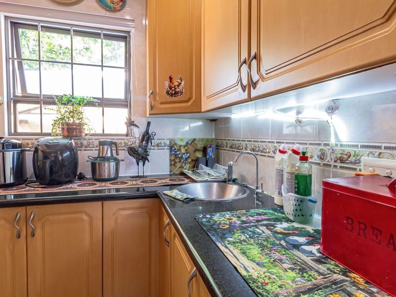 A compact kitchen featuring wood-finish cabinetry, dark granite countertops, a stainless steel sink, and a decorative tiled backsplash under a window.