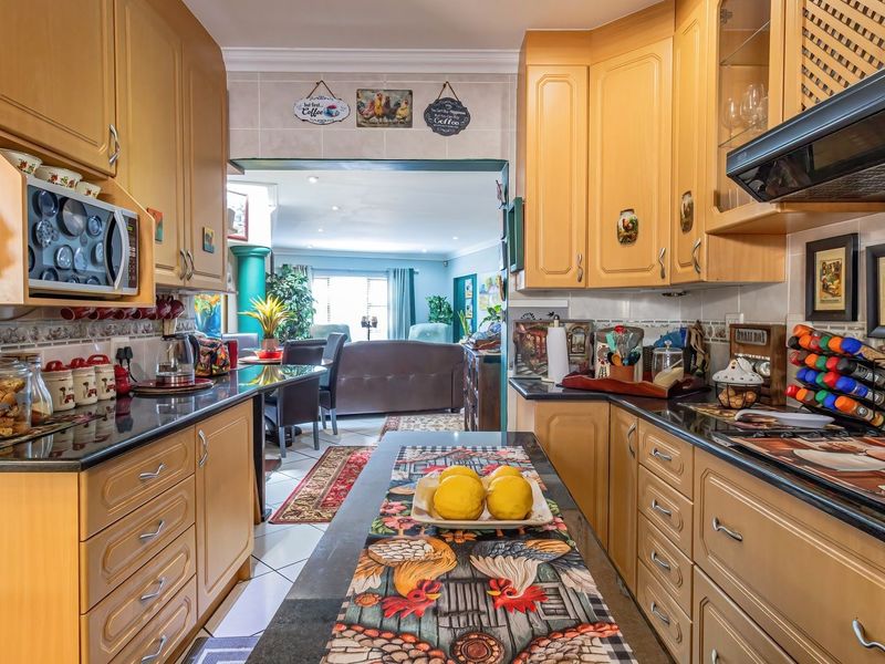 A functional kitchen featuring light wood cabinetry, dark granite countertops, and a built-in microwave, with an open-plan layout leading into the living area.