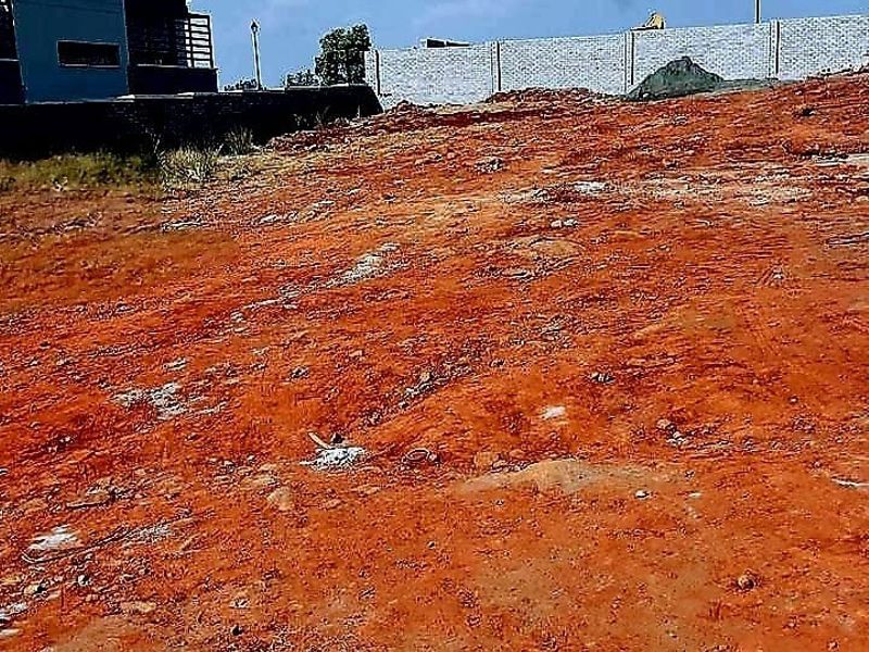 A view of a vacant residential plot featuring cleared red earth and a perimeter boundary wall.