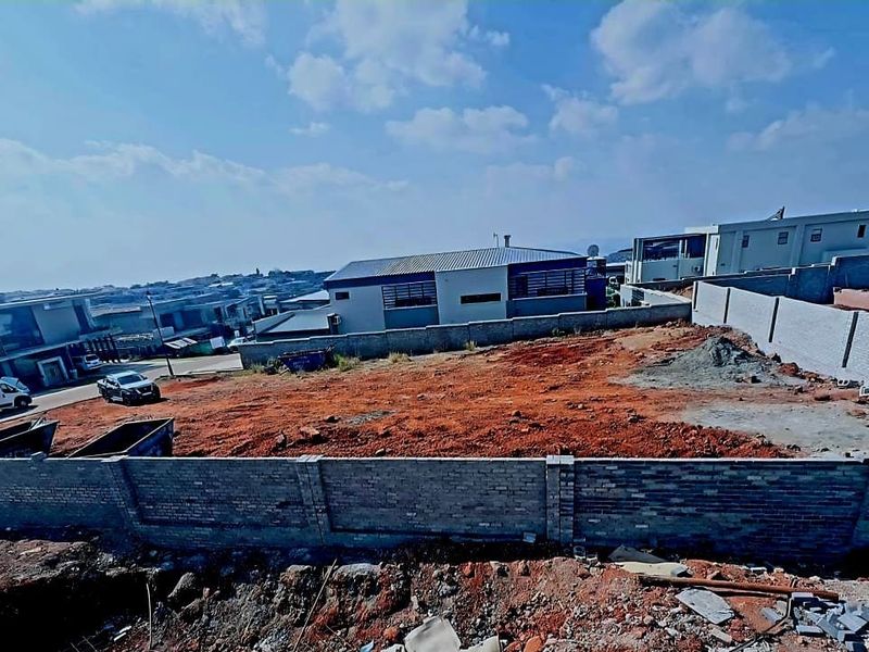 An elevated view of a vacant residential plot featuring a perimeter brick wall and cleared ground, situated within an established neighborhood.