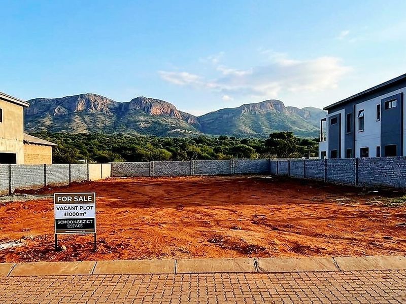 A vacant residential plot featuring a perimeter brick wall, paved street access, and scenic mountain views in a developed estate setting.