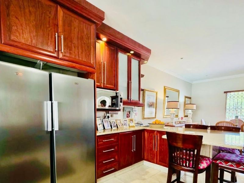 Open-plan kitchen and dining area featuring warm-toned wooden cabinetry, stone countertops, and integrated appliances, creating a functional and connected living space.