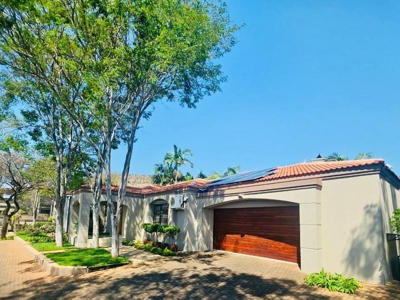 Front view of the property featuring a double garage, paved driveway, tiled roof with solar panels, and established trees in the front garden.