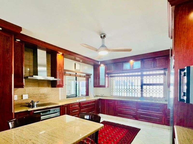 Spacious kitchen featuring extensive dark wood cabinetry, granite countertops, integrated appliances, and a ceiling fan, offering a classic and functional culinary workspace.