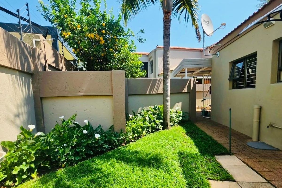 A well-maintained rear garden area featuring a paved walkway, perimeter wall with electric fencing, and established landscaping.