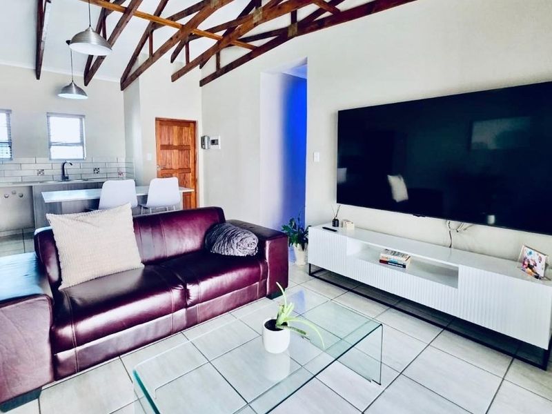 Open-plan living and kitchen area featuring high vaulted ceilings with exposed timber trusses, tiled flooring, and modern kitchen cabinetry.