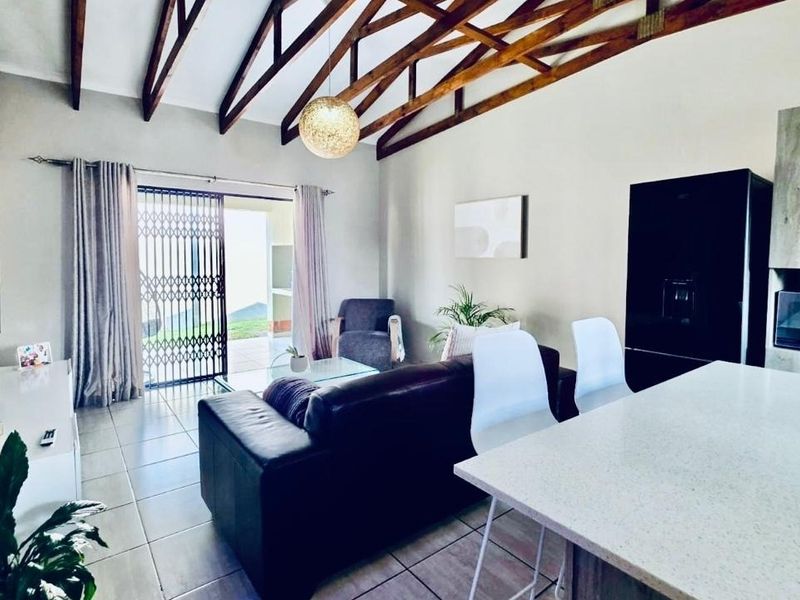 Open-plan living area featuring high vaulted ceilings with exposed timber trusses, a modern kitchen island, and direct access to an outdoor patio.