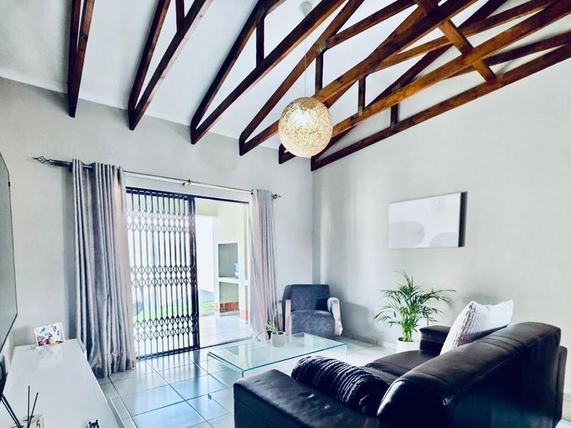 Spacious living room featuring high vaulted ceilings with exposed timber trusses, tiled flooring, and direct access to an outdoor patio through sliding glass doors.