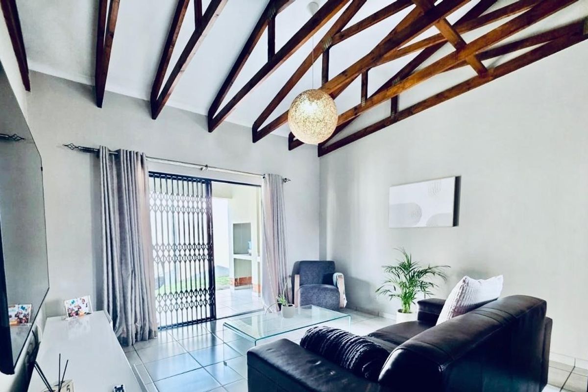 Spacious living room featuring high vaulted ceilings with exposed timber trusses, tiled flooring, and direct access to an outdoor patio through sliding glass doors.