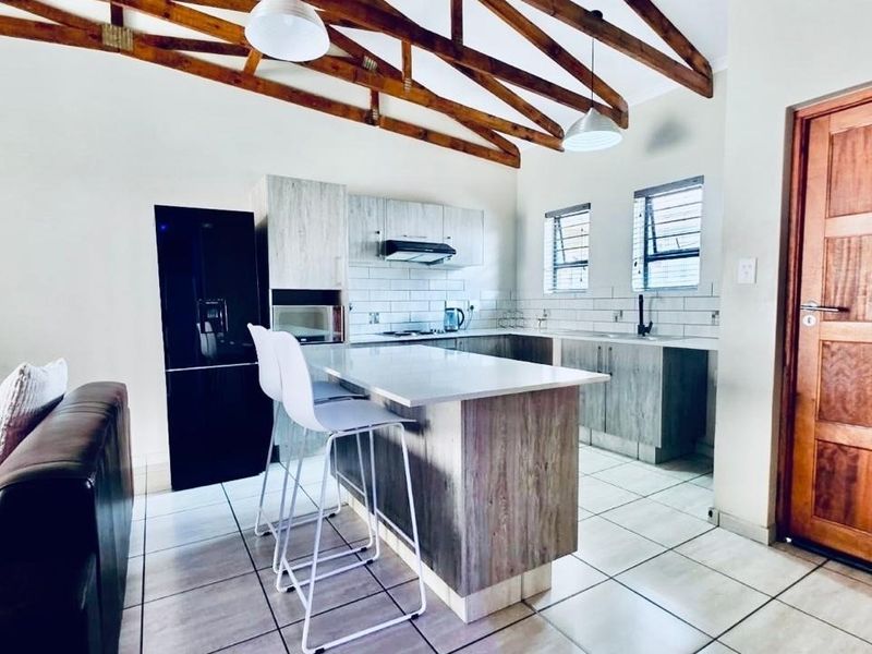 Open-plan kitchen and living area featuring exposed timber roof trusses, modern cabinetry, stone countertops, and a central island with breakfast bar seating.