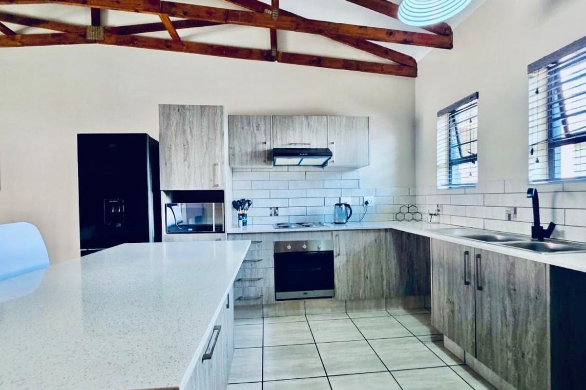 Modern kitchen featuring light wood-look cabinetry, quartz countertops, subway tile backsplash, and exposed timber roof trusses, creating a bright and contemporary cooking space.