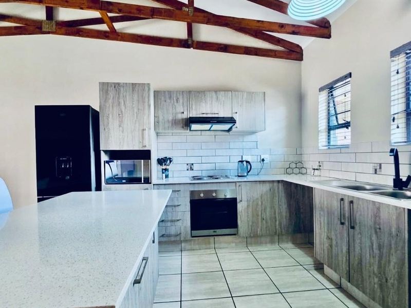 Modern kitchen featuring light wood-look cabinetry, quartz countertops, subway tile backsplash, and exposed timber roof trusses, creating a bright and contemporary cooking space.