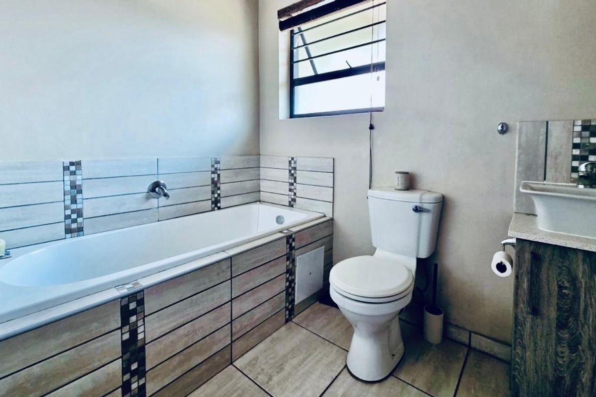A functional bathroom featuring a built-in bathtub with tiled surround, a toilet, and a vanity unit with a vessel sink.