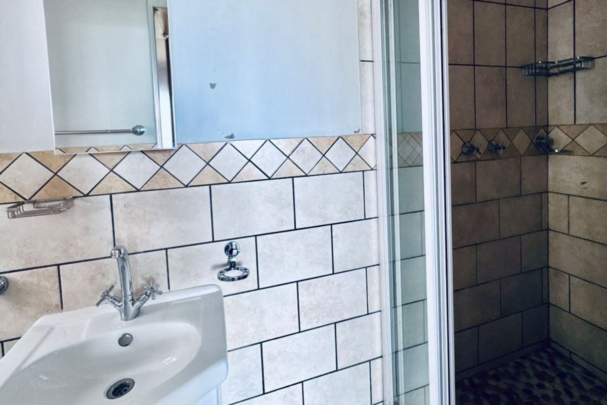 A functional bathroom featuring a pedestal basin, shower enclosure with tiled walls, and a wall-mounted mirror.