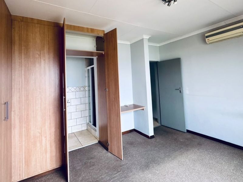 Spacious bedroom featuring built-in cupboards, a built-in desk, wall-mounted air conditioning, and direct access to an en-suite bathroom.