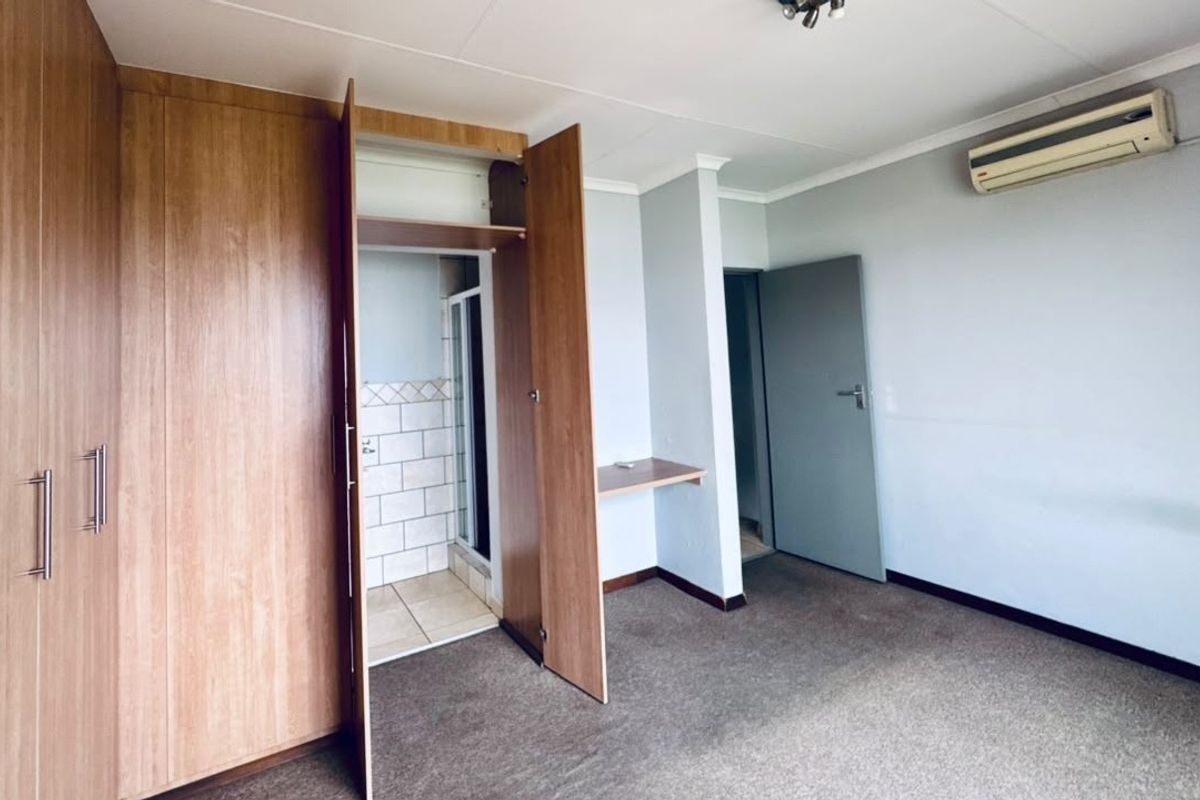 Spacious bedroom featuring built-in cupboards, a built-in desk, wall-mounted air conditioning, and direct access to an en-suite bathroom.