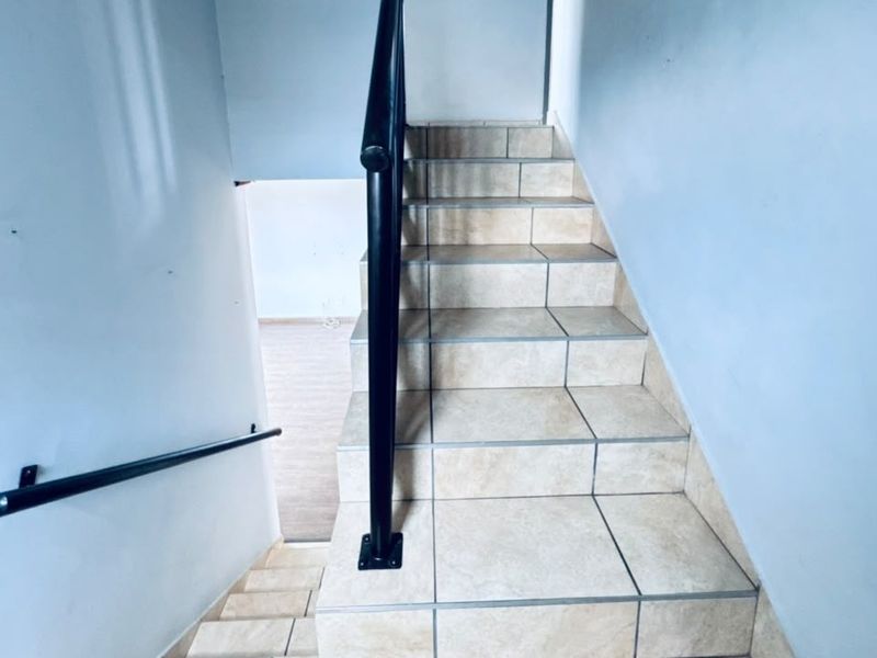 A functional staircase featuring tiled steps and black metal handrails, providing access between levels in the townhouse.