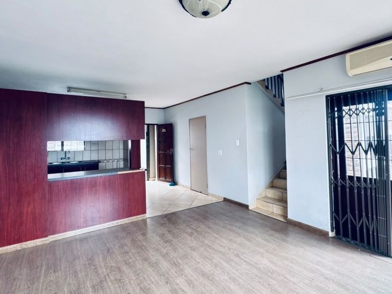 Open-plan living area featuring a kitchen with built-in cabinetry, staircase access, and a security gate leading to an outdoor balcony space.