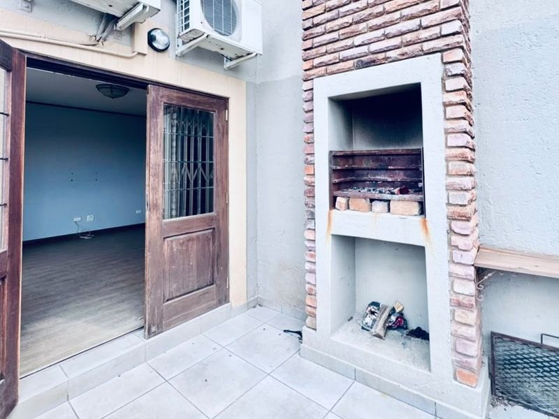Outdoor patio area featuring a built-in brick braai, tiled flooring, and direct access to the interior living space through double wooden doors.