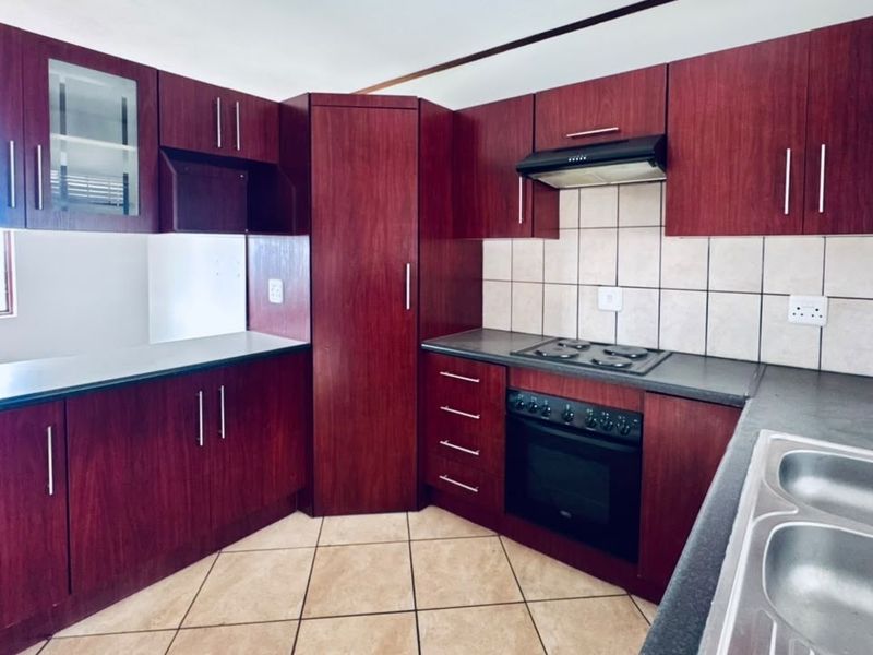 A functional kitchen featuring dark wood-finish cabinetry, built-in oven and hob, tiled backsplash, and ample counter space with a double bowl sink.
