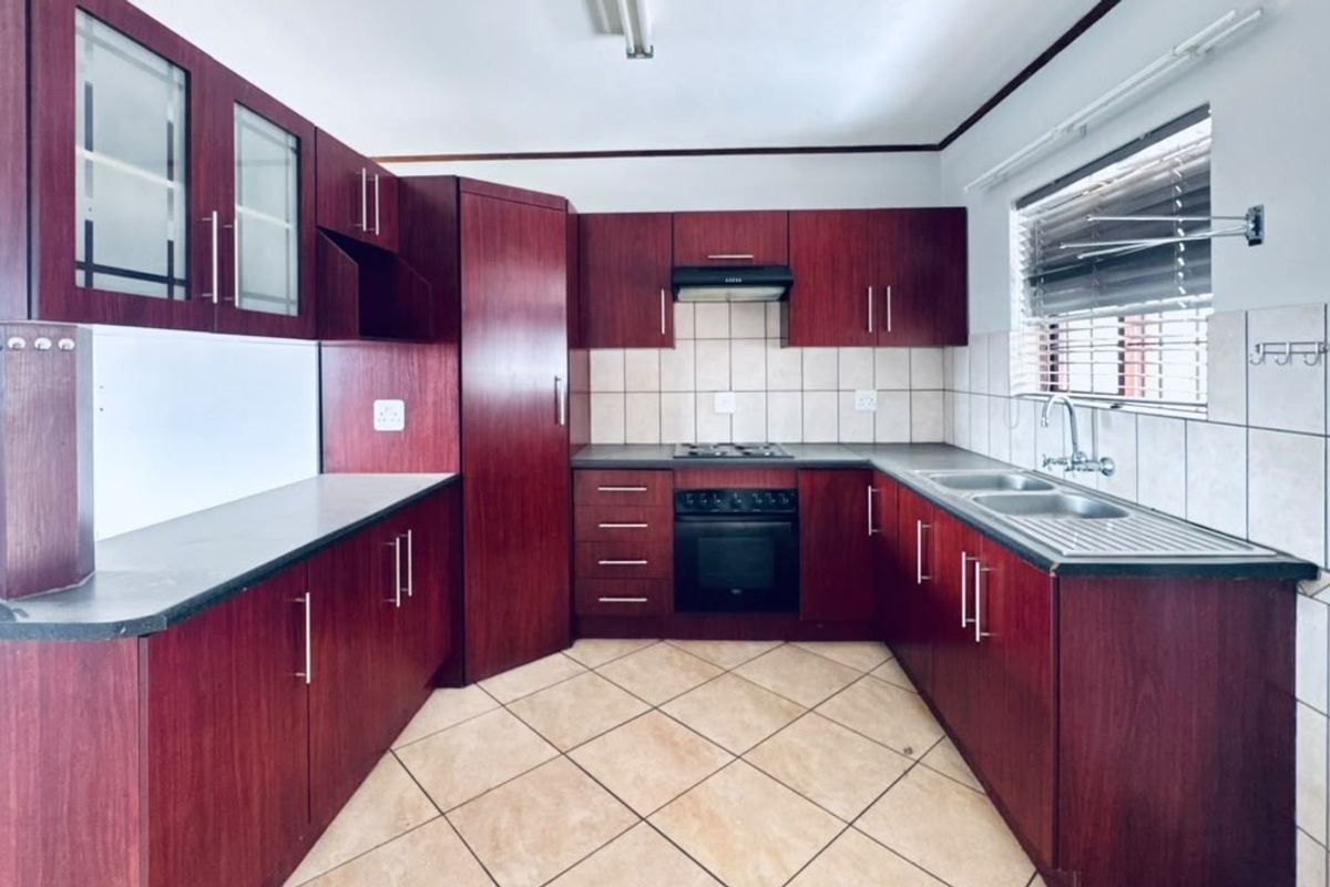 A functional kitchen featuring dark wood-finish cabinetry, built-in oven and hob, tiled backsplash, and double sink with ample counter space.