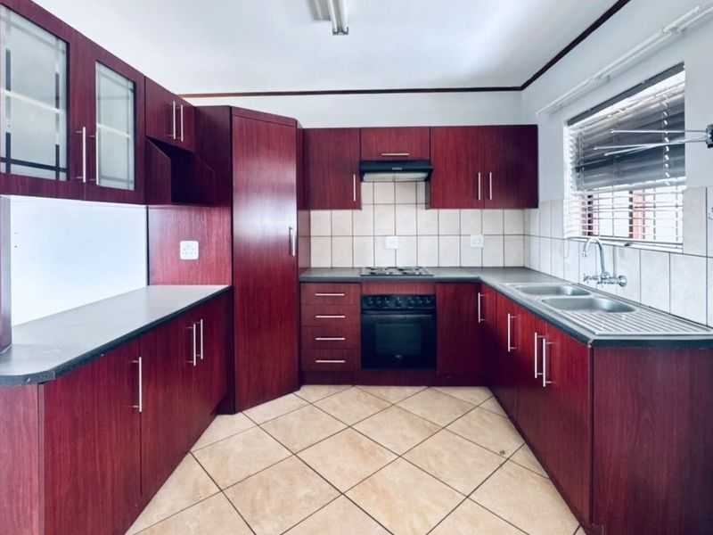 A functional kitchen featuring dark wood-finish cabinetry, built-in oven and hob, tiled backsplash, and double sink with ample counter space.