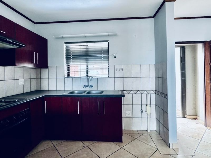 A functional kitchen featuring dark wood cabinetry, built-in oven and hob, double sink, and tiled splashbacks, offering a practical layout for daily use.