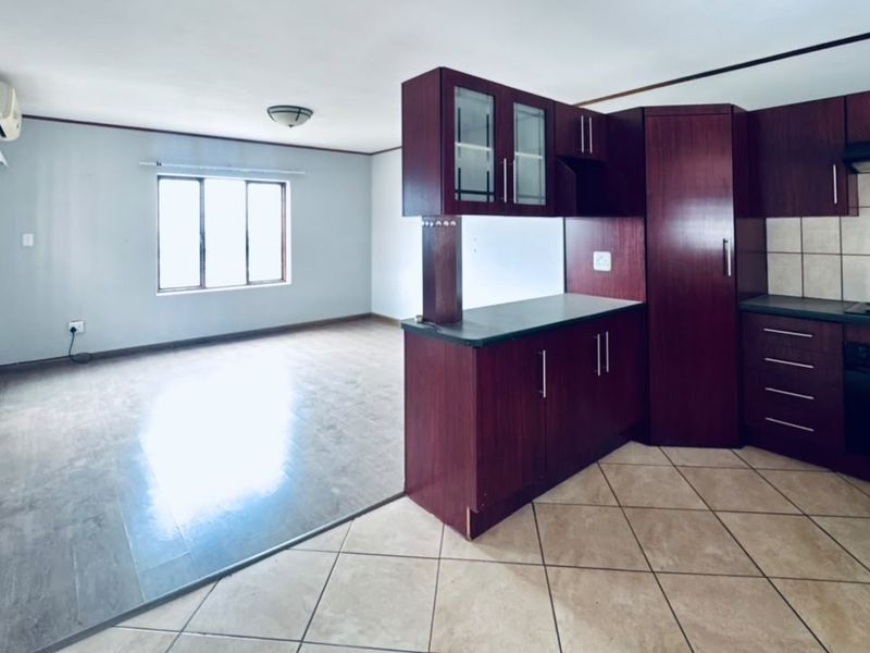 Open-plan living and kitchen area featuring dark wood cabinetry, built-in appliances, and a combination of tiled and laminate flooring.