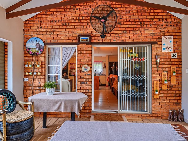 A covered patio area featuring exposed brick walls, timber ceiling beams, and a ceiling fan, providing a seamless transition to the interior living space.