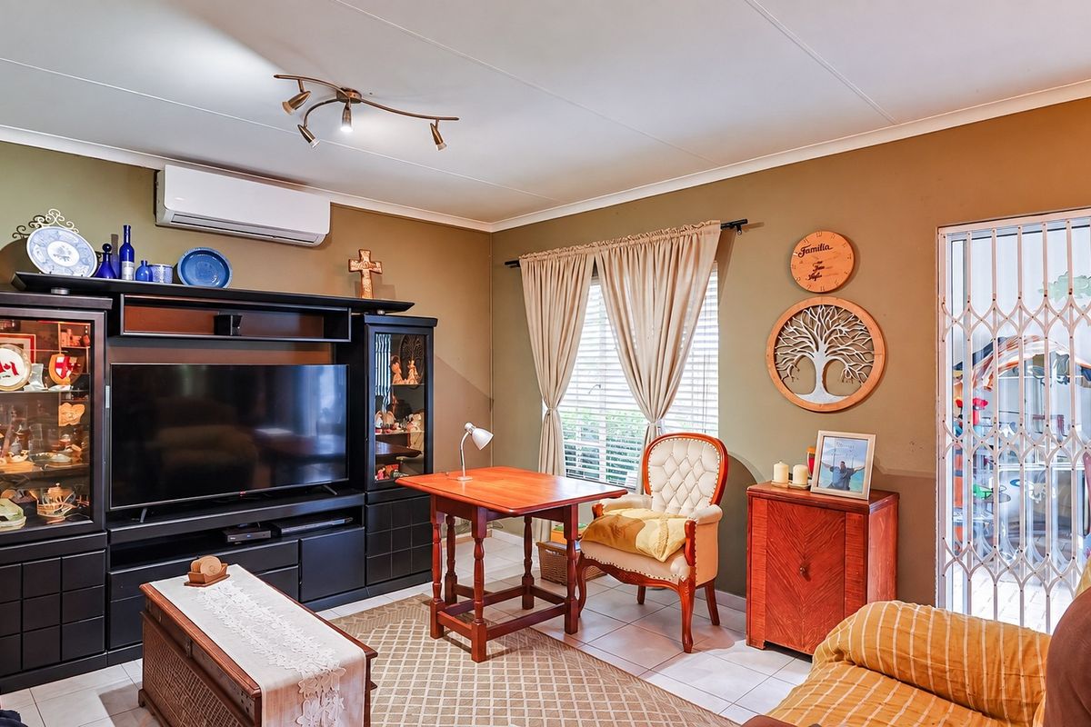 A living room featuring tiled flooring, a wall-mounted split-system air conditioner, and a security gate leading to an outdoor area.