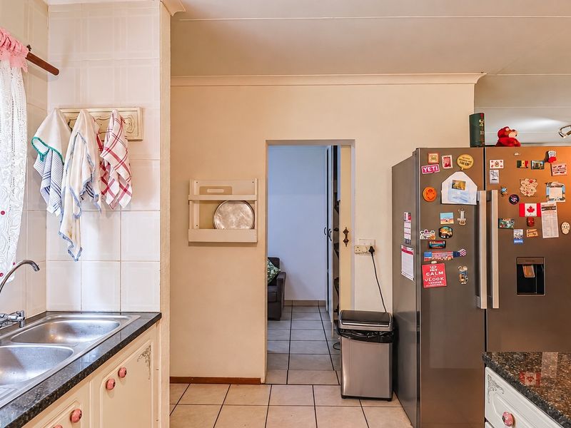 A functional kitchen featuring granite countertops, a double bowl stainless steel sink, tiled backsplash, and tiled flooring, with an open doorway leading to adjacent rooms.