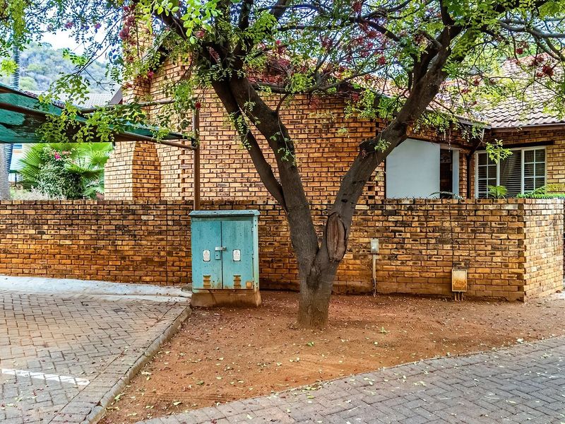 Front exterior view of a townhouse featuring a brick facade, paved driveway, and a shade cloth carport structure.