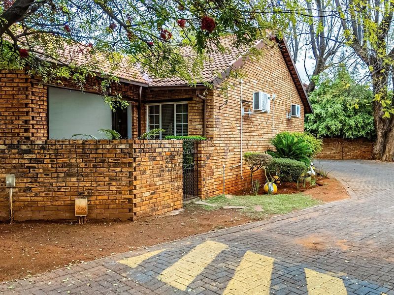Exterior view of a face-brick townhouse featuring a tiled roof, paved driveway, and established garden area with mounted air conditioning units.