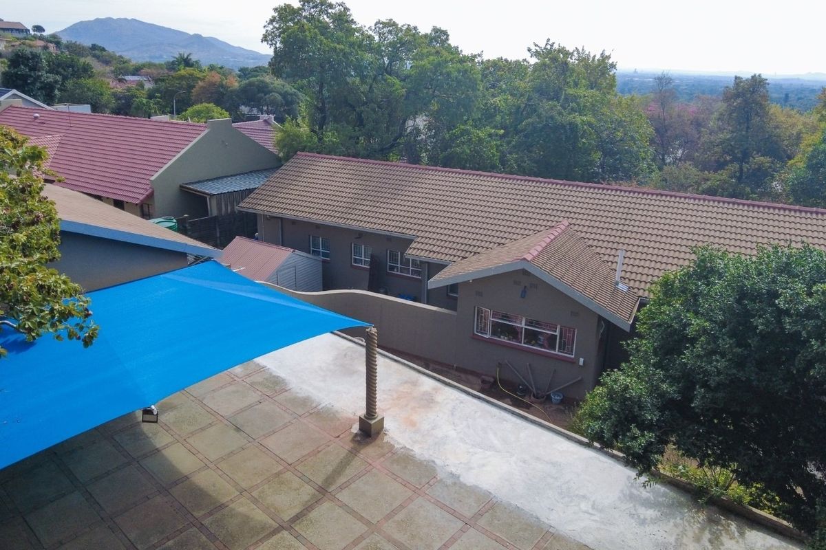 Aerial view of the property showing the tiled roof structure, paved patio area with a blue shade sail, and surrounding garden landscape.