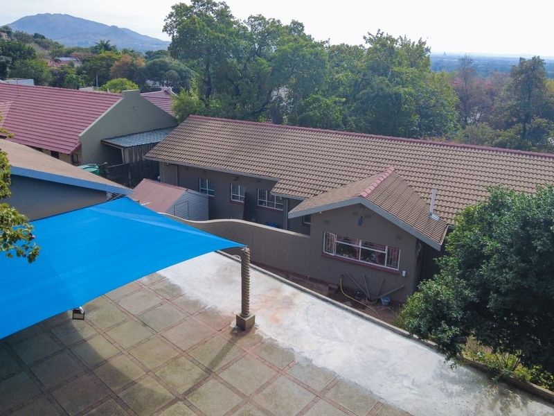 Aerial view of the property showing the tiled roof structure, paved patio area with a blue shade sail, and surrounding garden landscape.