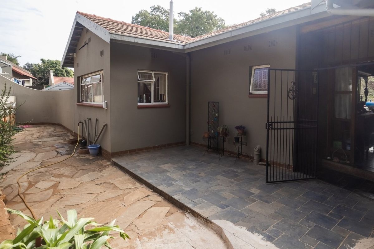 Rear exterior view featuring a tiled patio area, stone paved garden path, and secure gated access to the home.