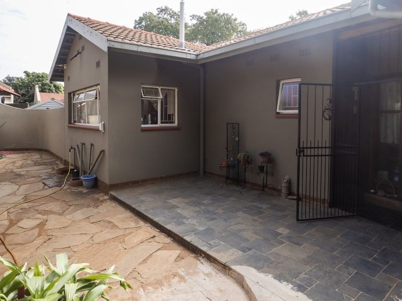Rear exterior view featuring a tiled patio area, stone paved garden path, and secure gated access to the home.
