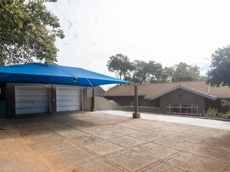 Front exterior view featuring a paved driveway, double garage with a blue shade sail, and a single-story house with a tiled roof.