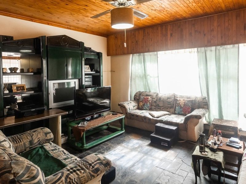 A living room featuring a distinctive timber-clad ceiling, ceiling fan, and dark stone tile flooring, offering a cozy and traditional aesthetic.