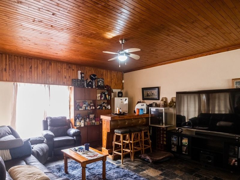 Spacious living room featuring a distinctive timber-clad ceiling and wall paneling, stone tile flooring, and a built-in bar area.