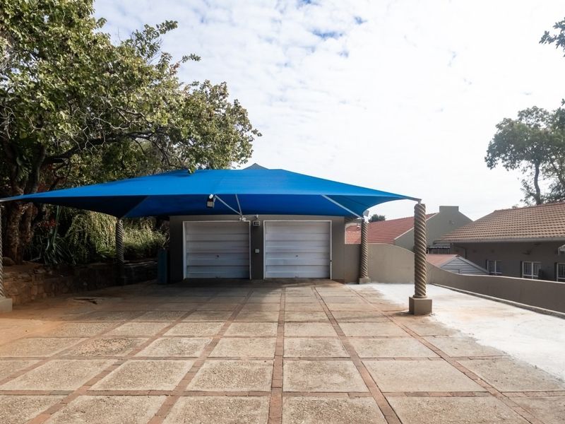 A double garage featuring a blue shade sail cover and a paved driveway area, set within a residential property.