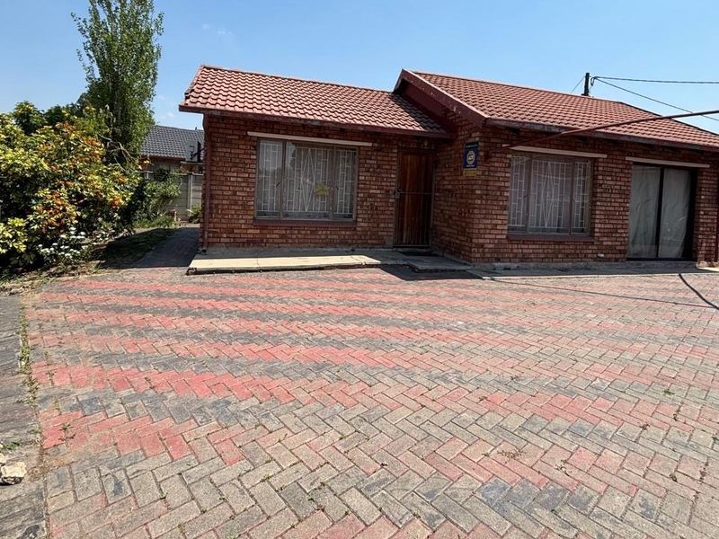 Front view of a face-brick house featuring a tiled roof and a spacious paved driveway with security features.