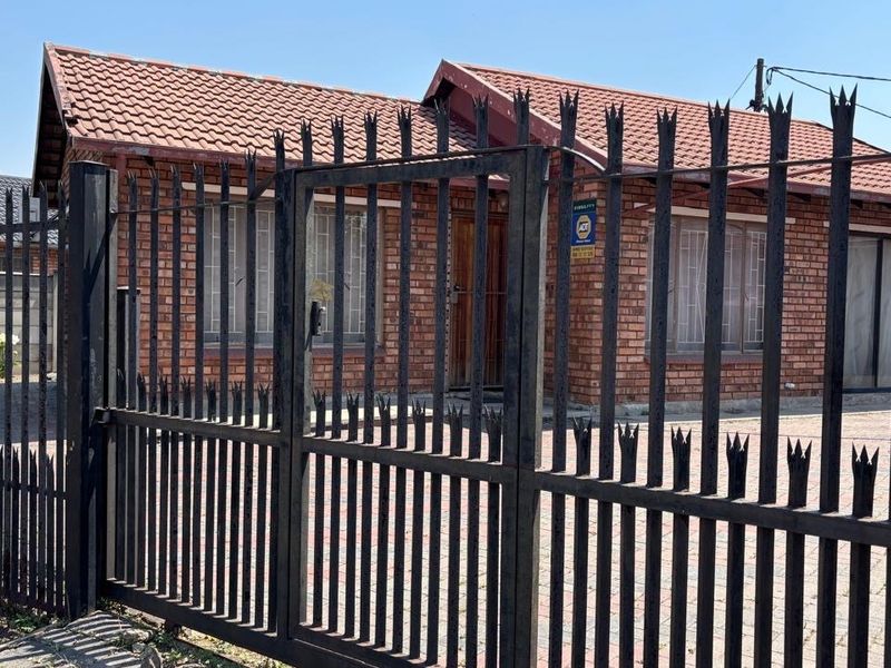 Front view of a face brick house featuring a tiled roof, paved driveway, and secure perimeter fencing with a metal gate.